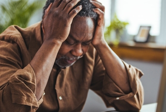 senior african american man sitting at table holding head in stress while looking at notebook