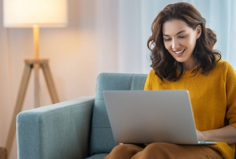A woman sitting on the couch in her living room, using her laptop.