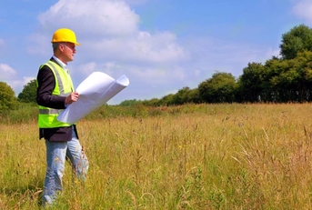 An architect in construction gear surving a new building plot.