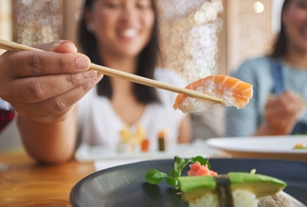 women eating sushi using chopstick