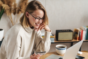 Smiling woman holding a credit card and looking at a computer