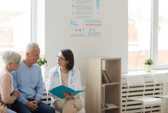 female doctor talking to senior couple while sitting in reception area of clinic