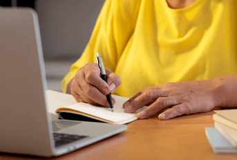 Senior woman writing note at desk with laptop