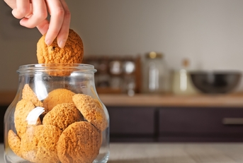 Woman taking oatmeal cookie from jar