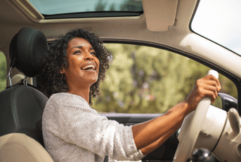 A woman grips the steering wheel and smiles while driving her car.