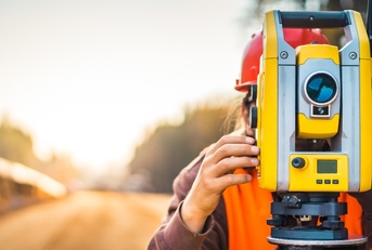 Person using large yellow surveyor camera zoomed with blurry background