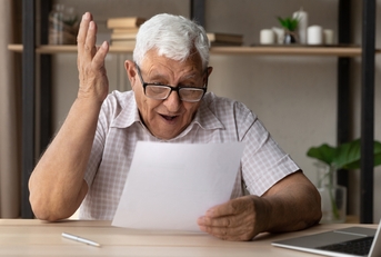 retired man in eyewear looking through paper document