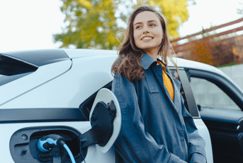 A woman leans against her electric car while it&#x27;s being charged.