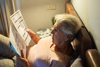 Worried senior woman reading bills in bed at night 