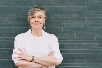 60-year-old woman in a cream blazer again a teal tile background