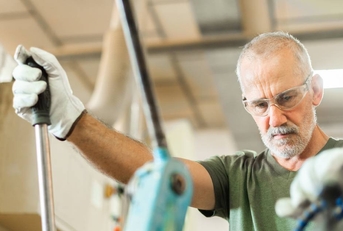 Older worker threading a steel bar in an industrial factory