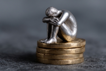 sad person silver figure sits atop of coins