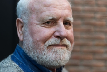 close up of a 70 year old man with a brick wall in the background
