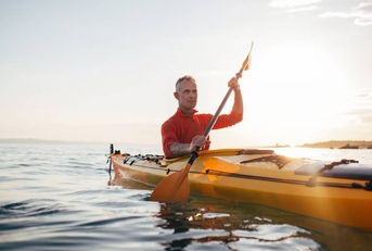 Senior man paddling kayak during sunset
