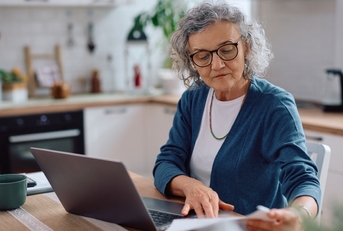 senior woman analyzing documents while using laptop