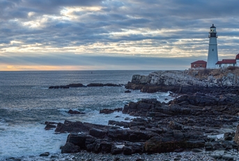 Maine lighthouse in background with ocean shoreline in foreground
