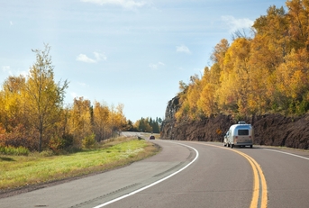 Minnesota road with trees on either side and a car pulling a trailer as the focus