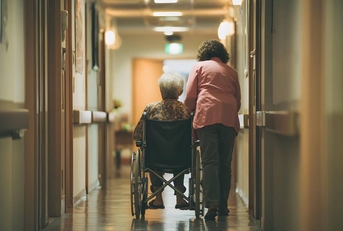Female Caregiver and Elderly Woman in Hospital Hallway