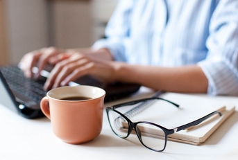 working on laptop with coffee, notebook, and glasses on table