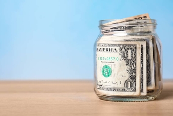 Jar with money on table against color background