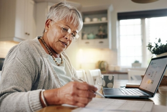 senior woman doing paperwork with laptop