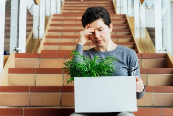 Woman with box of personal items sitting alone on the staircase after being laid off from job