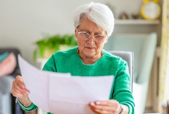 Older woman with white hair looking at paperwork worried