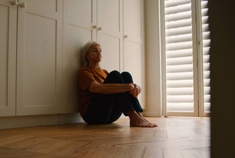 Sad Senior Woman Sitting On Floor At Home 