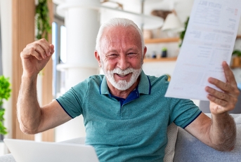 Older man happy smiling with arms up holding a paper