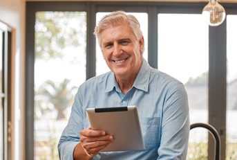 Man in his 60s smiling at the camera holding a tablet