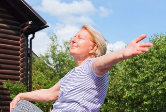 Woman sitting on the grass with open arms, enjoying the sunshine