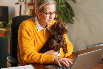 Woman sitting on a desk working from home holding her dog