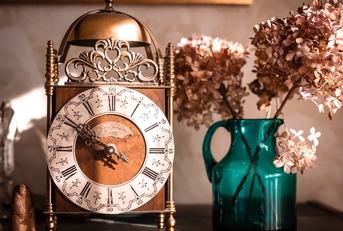 Old clock on the shelf next to flower vase