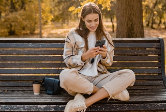 Woman sitting on bench using phone while smiling