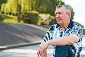 Man in his 50s sitting outdoors looking beyond, thinking