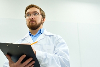 Man wearing lab coat taking notes 