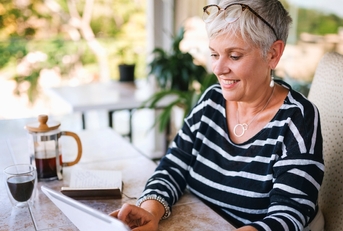 Woman with short, white hair sitting at the table reading a letter and having coffee