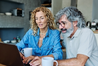 Couple in their 60s sitting at home having coffee and looking at notebook