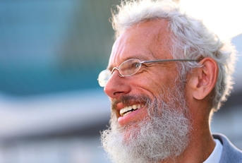 Man with white hair and beard wearing glasses and smiling