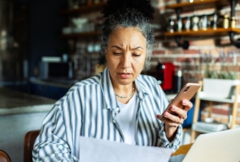 Mature woman on laptop and phone with worried expression