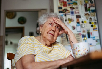 Portrait of worried senior woman sitting in kitchen. 
