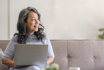 Smiling woman in 60s on couch with laptop