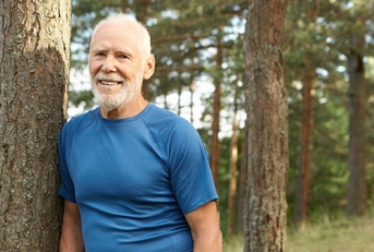 Smiling older man leaning against a tree