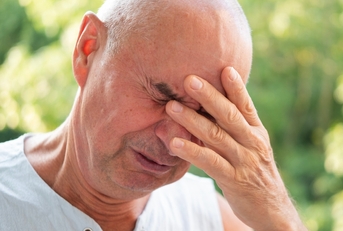 Man in his sixties looking worried with eyes closed and hand on his face
