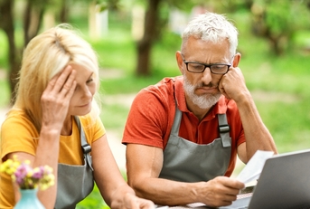 Retired couple sitting outside looking over finances worried faces