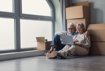 Older couple sitting against moving boxes with laptop