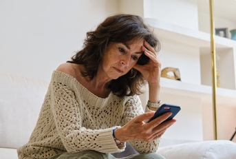 Concerned mature woman on couch looking at phone