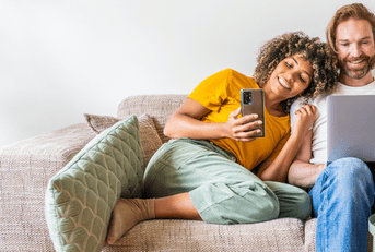 Young couple sitting on couch looking at phone and laptop