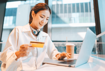 Gen Z woman at cafe on laptop wth debit card in hand