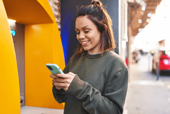 Young woman on mobile phone using outdoor ATM
